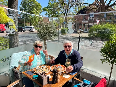 Gäste mit Pizza und Aperol Spritz auf der sonnigen Terrasse